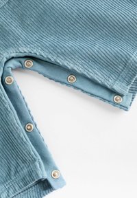 Blue, ribbed fabric featuring metallic snaps along the edge of a garment, with a soft, textured visual appearance and clean design.