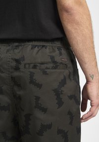 Ciemnozielone szorty z czarnym wzorem nietoperzy, z elastyczną talią i jedną tylną kieszenią. Dyskretny logo marki na kieszeni.