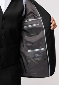 Wnętrze czarnego żakietu ma szare podszewki z subtelnymi wzorami, liczne kieszenie oraz metki marki, w tym Roy Robson i Reda 1865.