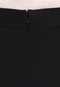 Svart stretchig kjol med en synlig dragkedja bak, som har en slät yta och en figurnära passform. Enkel och minimalisk design.