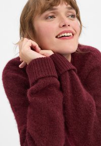 Burgundy sweater made of soft, textured material with ribbed cuffs, featuring a relaxed fit and slightly oversized design.