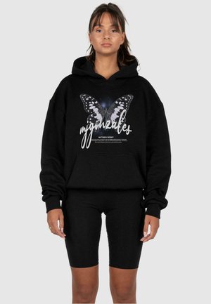 Schwarzer Kapuzenpullover mit einem Schmetterlings-Design und Text, ausgestattet mit einer geräumigen Fronttasche und lockerem Schnitt, kombiniert mit schwarzen Radshorts.