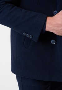 Marineblaue Wollmischungjacke mit strukturiertem Oberflächen, Knopfmanschetten und taillierter Passform sowie Seitentaschen.