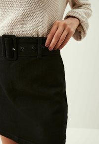 Gonna in denim nera con una cintura larga e una fibbia rettangolare, cinque passanti per la cintura e una superficie liscia. Design casual con una forma aderente.