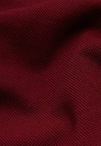 Burgundowa dzianina teksturowana w wzór gofrowy, gładkie wykończenie, delikatnie opadająca, podkreślająca głębię i kontury materiału.