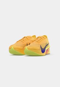 Baskets de sport jaunes éclatantes avec un dessus texturé, un logo swoosh violet et une semelle extérieure verte. Le design léger améliore les performances.