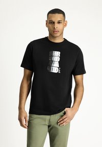 T-shirt in cotone nero con audace scritta bianca e grigia impilata sul davanti. Maniche corte e scollatura tonda.