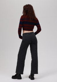 Cropped, striped sweater in dark red and navy, paired with high-waisted black wide-leg jeans. Model wears black platform boots.