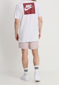 Vaaleanharmaa t-paita, jossa takana on maroon Nike-logo, jossa lukee "AIR", yhdistettynä vaaleanpunaisiin shortseihin ja valkoisiin lenkkikenkiin mustilla raidoilla.