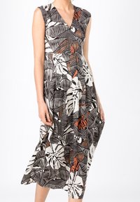 Robe avec un décolleté en V, sans manches. Présente un motif de feuilles noir, blanc et rouille. Tissu fluide, longueur genoux.