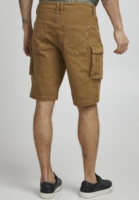 Brown cargo shorts with side pockets, made from durable cotton material. Features a relaxed fit and stitching details on the back pockets.