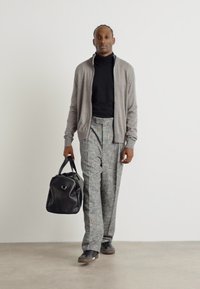 Grå kofta, svart turtleneck, grå mönstrade byxor, svart duffelväska och skor. Enkelt design med släta texturer och skräddarsydd passform.
