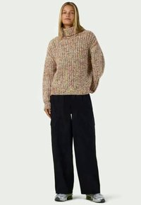 Suéter de malha grossa em fio multicolorido com gola alta. Combinado com calças cargo pretas de corte largo e ténis cinzentos.