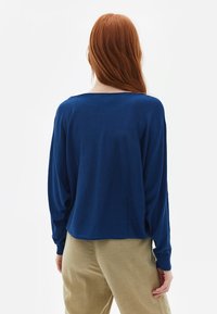 Blauwe gebreide trui met lange, losse mouwen en een wijd uitgesneden halslijn. Zachte textuur, middellange snit, gecombineerd met lichtbeige broeken.