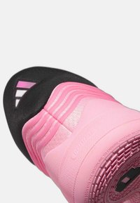 Pink athletic shoe with textured design, black toe cap, and ridged accents. Features a textured sole and prominent logo on the side.
