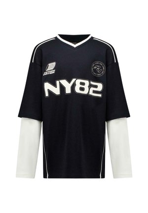 Zwart langermig gelaagd shirt met witte mouwen, "NY82" tekst in vet wit, en kleine witte logo's op borst en schouders.