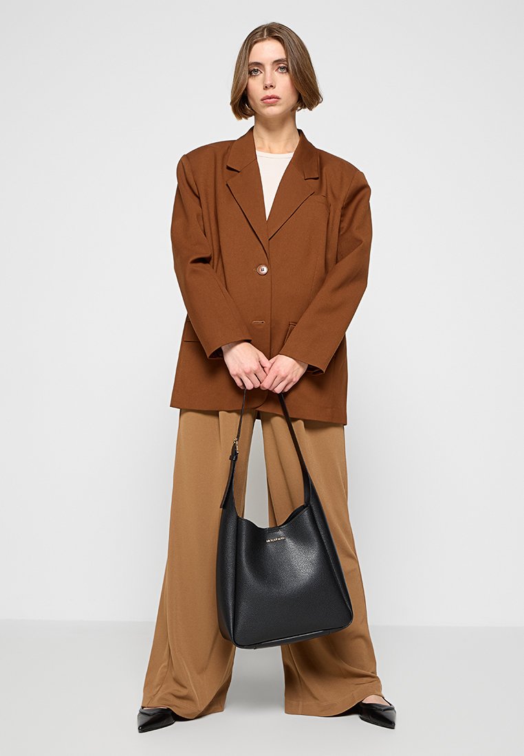Brauner übergroßer Blazer mit einem Knopf, beiger weit geschnittener Hose und einer strukturierten schwarzen Handtasche mit Schulterriemen. Schwarze spitze Schuhe.