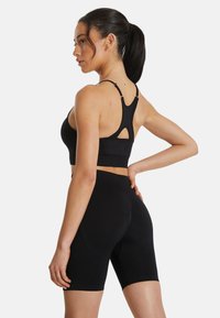 Zwarte sportbeha met een racerback ontwerp en uitsnijdetail, gecombineerd met zwarte hoge taille fietsshorts met een gladde textuur en een aansluitende pasvorm.