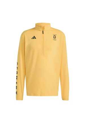 Gul långärmad tröja med halvdragkedja och krage, med svart "TEAM D" och Olympiska ringar-logotyp, samt texten "GERMANY" på ärmen.