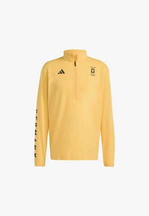 Gul långärmad tröja med halvdragkedja och krage, med svart "TEAM D" och Olympiska ringar-logotyp, samt texten "GERMANY" på ärmen.