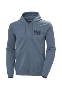 Sudadera azul con cremallera, hecha de un tejido suave, que cuenta con un bolsillo tipo canguro, puños acanalados y un logo de Helly Hansen en el pecho. Textura suave.