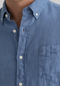 Camicia button-up azzurro chiaro realizzata in un tessuto texturizzato. Presenta un colletto, una piccola tasca con logo e chiusure a bottoni bianchi.