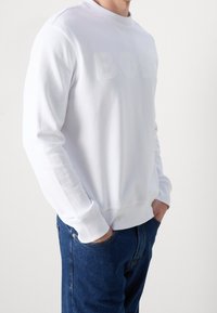 Vit sweatshirt med präglad "BOSS" logotyp, rundad hals och ribbade muddvidder, tillsammans med blå denimjeans. Slät yta, avslappnad passform.