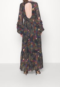 Robe longue et transparente avec une découpe profonde dans le dos, ornée de motifs floraux colorés sur un fond noir. Manches à volants et ourlet à étages.