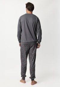 Sudadera gris para hombre y pantalones de pijama con un diseño estampado. Los pantalones presentan un diseño floral en rojo y verde sobre un fondo gris.