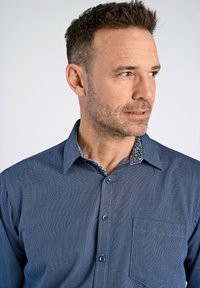 Tummansininen napitettu paita, jossa on teksturoitu kangas, kontrastivärinen kuvioitu sisäkaulus ja yksi rintatasku. Varustettu sinisillä nappeilla.
