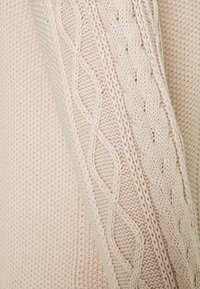 Pull en tricot rose clair avec un motif en câble texturé sur les manches et le corps ; présente des bords côtes et un fil doux et épais.