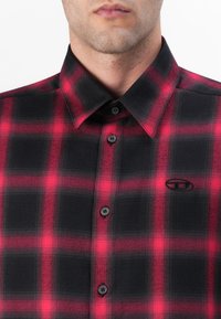 Camisa de cuadros en rojo y negro, material de algodón, estilo de botones, con un cuello clásico y un pequeño logo en el pecho.