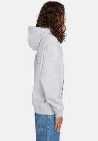 Sudadera con capucha gris de corte relajado, hecha de una tela suave, con un bolsillo tipo canguro, puños y dobladillo acanalados, y un discreto detalle de logo.