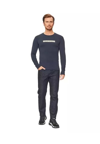 Camicia a maniche lunghe blu navy con un'etichetta logo sul petto, abbinata a pantaloni in denim scuro e scarpe da ginnastica nere. Design aderente.