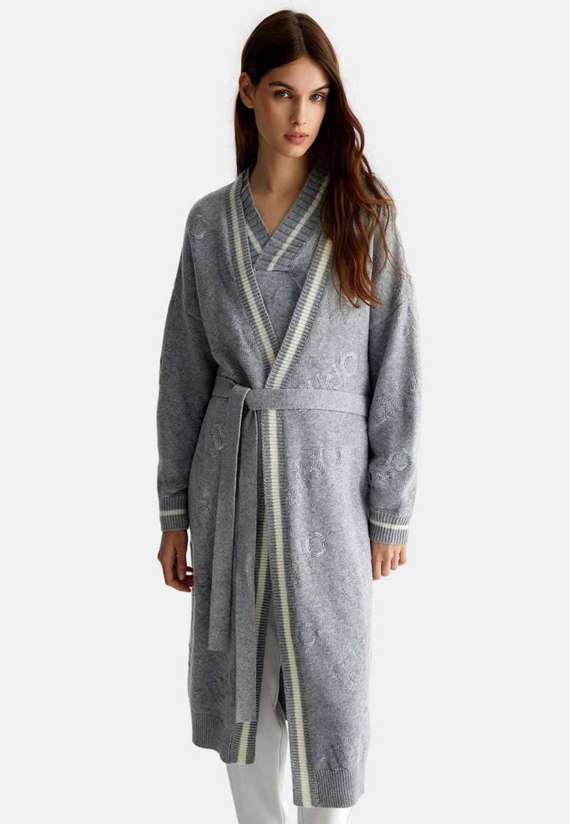 Accappatoio grigio a maglia con colletto a scialle, vita aderente e polsini a costine. Presenta una sottile texture e leggeri accenti a righe lungo i bordi.