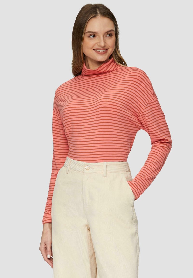 Langarm-Turtleneck-Shirt in gestreiftem Korallen- und Pinkton, mit einer lockeren Passform und weichem Stoff, kombiniert mit cremefarbenen Cordhosen.