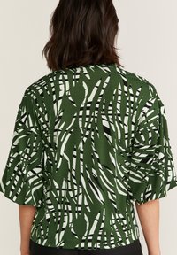 Blusa verde a fantasia con strisce astratte in bianco e nero. Realizzata in tessuto morbido, presenta maniche corte e larghe e una vestibilità rilassata.