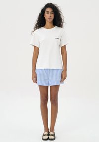 Biała bawełniana koszulka z krótkim rękawem i małym czarnym logo. Połączona z jasnoniebieskimi spodniami w paski i czarnymi butami bez zapięcia.