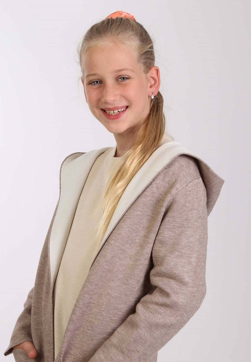 Cardigan marron clair avec une capuche blanche, texture douce, manches longues et poches avant, porté sur une chemise beige.