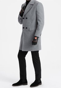 Šedý kabát z vlněné směsi s dvouřadým zapínáním na černé knoflíky, boční kapsy, v páru s černými kalhotami a odpovídajícími kotníkovými botami. Černé rukavice bez prstů.