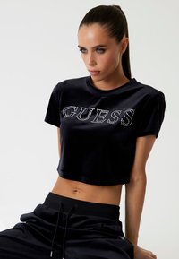 Juodas trumpas veliūro marškinėliai su žvilgančiais stikliukais, užrašytas žodžiu "GUESS". Trumpomis rankovėmis ir apvaliu kaklu.