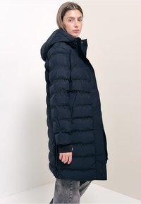 Námořnický modrý péřový kabát s kapucí, zdobený prošívaným vzorem, dlouhými rukávy, bočními kapsami a rovnými liniemi sahajícími do poloviny stehna.