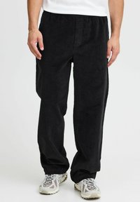 Black corduroy pants with a relaxed fit and elastic waistband, featuring vertical ribbing texture and side pockets. Worn with light-colored sneakers.