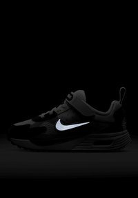 Sneaker preto infantil com detalhes cinzas, swoosh refletivo da Nike, fita de velcro e alça em um fundo escuro.