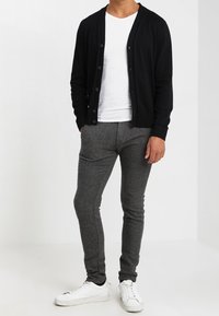 Černý cardigan s knoflíky, zkombinovaný s bílým tričkem. Šedé přiléhavé kalhoty a bílé tenisky. Hladká textura celého outfitu.