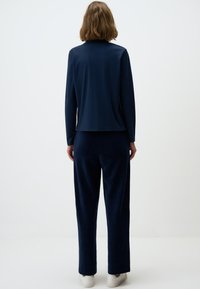 Navyblauwe relaxte top met lange mouwen en een iets verkorte snit, gecombineerd met bijpassende fluwelen broek en witte sneakers.