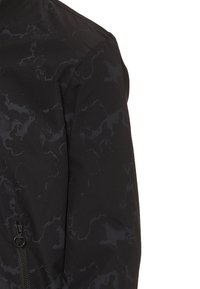 Zwarte jas met een gestructureerd patroon, ritszakdetails en een getailleerd design. Materiaal lijkt glad met een subtiele glans.