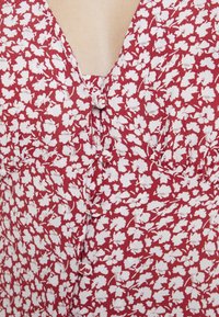 Rode bloemen jurk met klein wit bloemenpatroon, v-halslijn en knoopdetail in het midden. Gemaakt van lichte, gestructureerde stof.