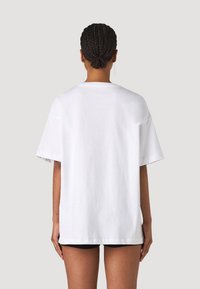 Camiseta de algodón blanca de corte oversize con mangas cortas, escote redondo y un ajuste relajado. Detalles de costura en los hombros y un respaldo liso.