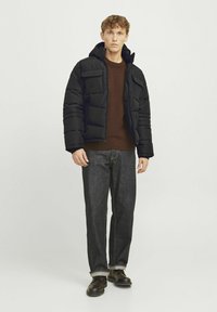 Sort puffjakke med hætte og to frontlommer, båret over en brun sweater og parret med mørke denim jeans og brune sko.